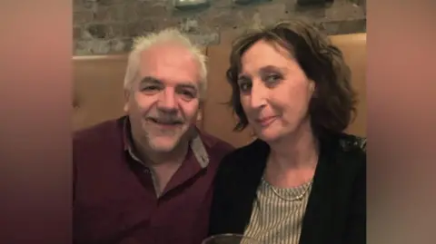 PA Media A husband and wife sitting at a restaurant looking at the camera.
There is a glass of white wine in the frame. They are sitting down 