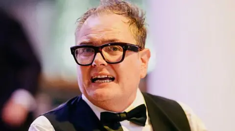 Getty Images Comedian Alan Carr with his trademark large, dark glasses with a black bow tie, waistcoat and white shirt