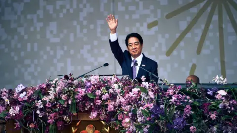 Getty Images William Lai, de traje, saluda a la multitud con el brazo mientras está en el escenario.