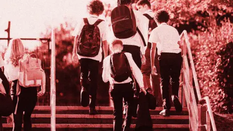 Photo of six teenage schoolchildren walking up steps. They are wearing dark trousers and skirts, with white shirts. Some are carrying rucksacks on their backs. 