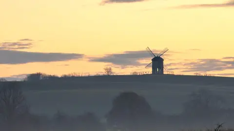 Damien Walmsley A windmill on a hill during an early morning sunrise.