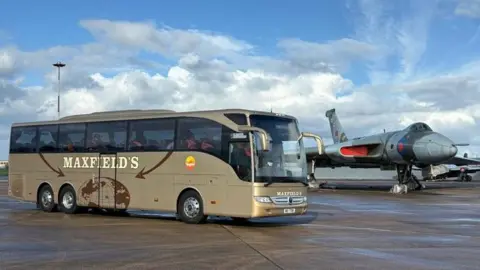 Maxfield's Travel Gold and brown Maxfield's bus parked next to a grey, green and red aeroplane