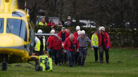 Edale Mountain Rescue Team Members of the rescue team, wearing red jackets, carry a casualty on a stretch towards a yellow air ambulance helicopter