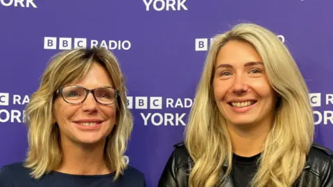 BBC/ELLY FIORENTINI Chocolate and Co founders - and mum and daughter - Linda Barrie (left) and Mariah Pape, are pictured at BBC Radio York's Make a Difference Awards after winning the Community Group category. They both have blonde hair and are smiling at the camera.