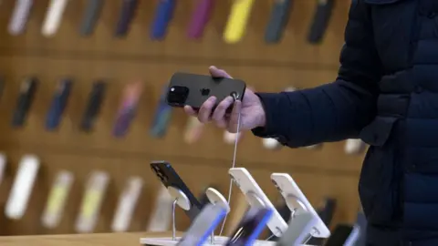 Getty Images A hand holds a black iPhone in an iPhone store