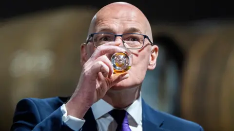 PA Media John Swinney tastes a single malt whisky at the Deanston Distillery, near Doune