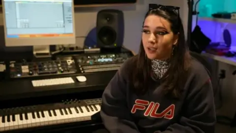 Rebecca Searle sitting next to a keyboard in a music studio