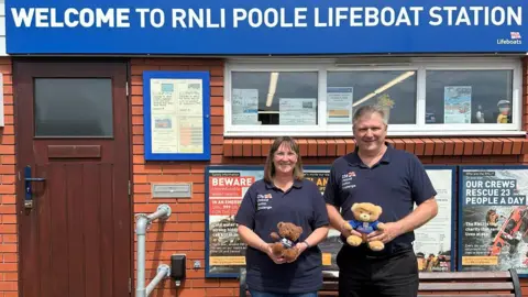 Two people holding small toy bears outside Poole lifeboat station building