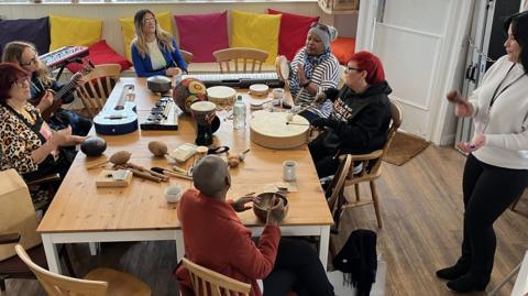 Six women sat around a table playing different instruments