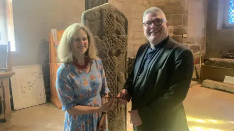 Church of Scotland Two people standing beside a large carved stone cross inside a cathedral. Both people are facing the camera and are holding a large key.