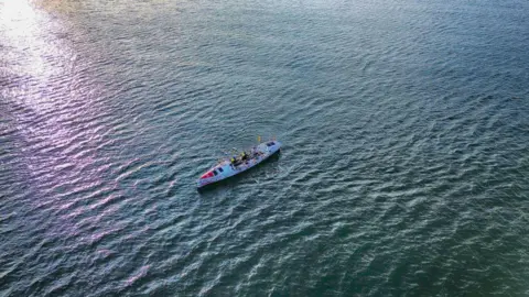 A drone image of a lone rowing boat in the middle of the ocean.