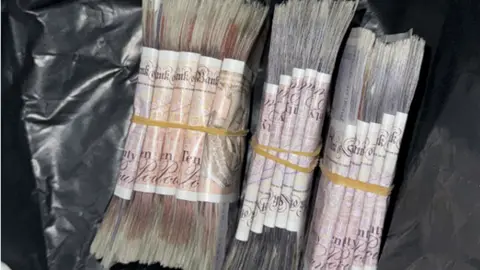 Avon and Somerset Police Bundles of cash lie on top of a plastic sheet