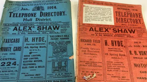 Two old telephone directories side-by-side. A blue one dated 1914 and a red one dated 1918
