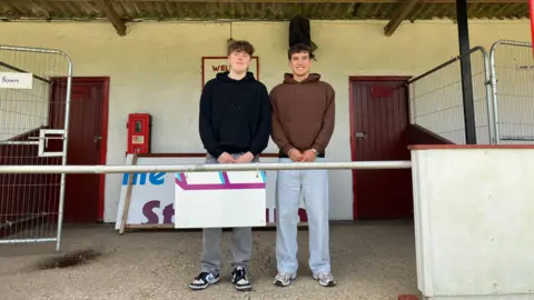 Tom Gough and George Callie outside a football changing area. They are both wearing hoodies.