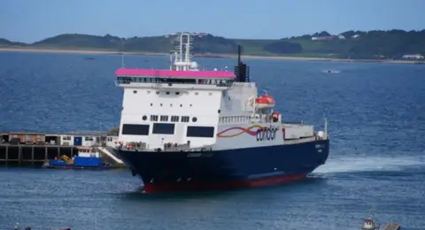 A wide shot of Commodore Goodwill entering a harbour. It is big a white, with a navy blue underside.