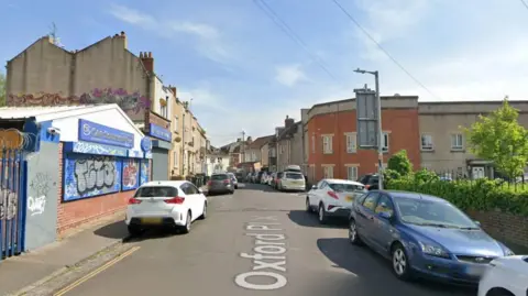 A Google Maps screengrab of Oxford Place in Easton, Bristol, a narrow residential street lined with parked cars with a garage on the corner. 