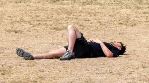 A man lies on his back on parched, brown grass