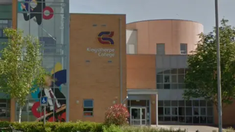A Google Maps street view image of the outside of Kingsthorpe College. It is a modular style building with the Kingsthorpe College logo on it.