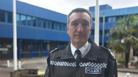 Steve Cooper is pictured outside force HQ wearing a black jacket bearing a badge that says "Police"