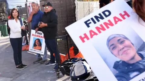 People crowd around missing person flyers showing Hannah Kobayashi 