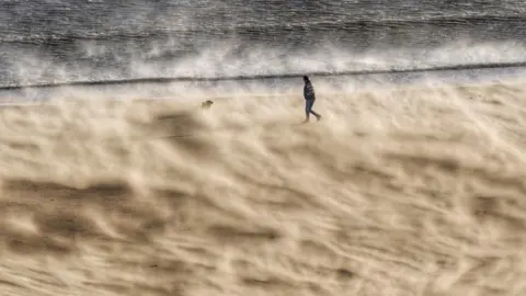 PA Media A walker battles strong winds at Tynemouth beach