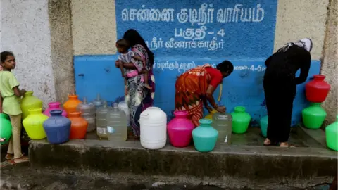 R Parthabhan Indian residents stand around with plastic pots filled with drinking water at a distribution point in Chennai on June 20, 2019. - Water levels in the four main reservoirs in Chennai have fallen to one of its lowest levels in 70 years, according to Indian media reports