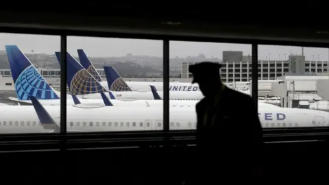 Getty Images A pilot, in silhouette, walks by United Airlines planes as they sit parked at gates at San Francisco International Airport.