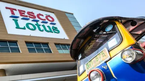 Getty Images A Thailand's traditional Tuk Tuk waits for customers outside a Tesco-Lotus supermarket in Bangkok.