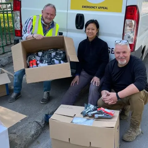 Kev Draper Kev Draper (left) with two other volunteer helpers sitting with cardboard boxes with equipment in front of a van