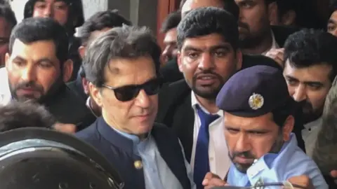 AFP Imran Khan leaving court on Friday. He is wearing sunglasses and making his way through a crowd of people.