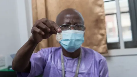 MRC Unit The Gambia at LSHTM A healthcare worker in The Gambia holds up a microarray patch of the type used in the study.