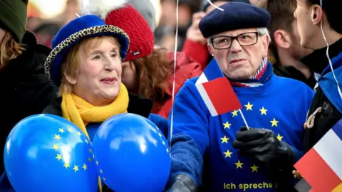EPA A man and woman dressed int eh bright blue and yellow colours of the EU stand at a barrier, holding balloons and the French flag on a stick
