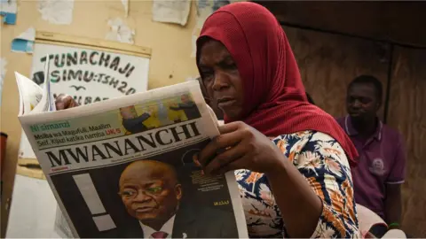 AFP A woman reads a newspaper announcing the death of Tanzania's President John Magufuli in Dar es Salaam, on March 18, 2021.