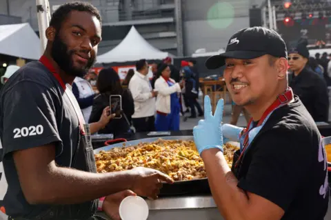 JEFF SCHEAR/GETTY IMAGES A view of The Simple Art of Rice's Liberian Jollof being prepared during the Food Network New York City Wine & Food Festival presented by Capital One - Bacardi presents The Cookout: Hip Hop's 50th Anniversary Celebration featuring DJ CASSIDY, JJ Johnson, Rev Run, Ice-T, DJ MICK, Tamron Hall & Angela Yee at Pier 86 on October 15, 2023 in New York City. (Photo by Jeff Schear/Getty Images for NYCWFF)