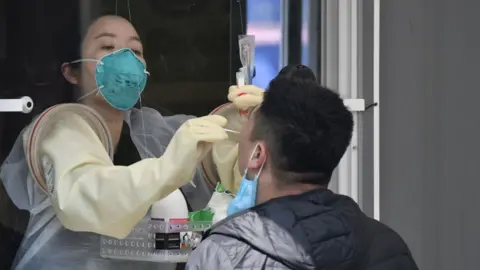 Getty Images A woman wearing a mask doing a throat swab on a man through a window