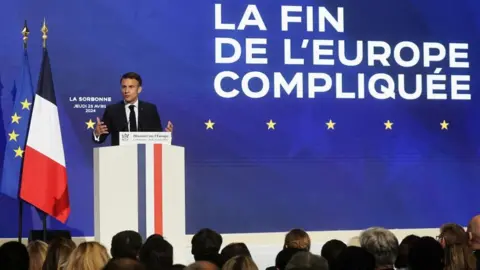 Christophe Petit Tesson/Pool via REUTERS French President Emmanuel Macron delivers a speech on Europe next to a slogan reading 'The end of a complicated Europe'