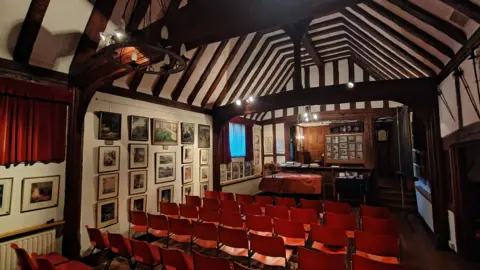 Simon Furber/BBC A billiard room, with several rows of red chairs. There are paintings hung on the wall.