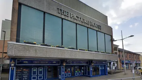 Exterior view of The Picture House building on Bethcar Street in Ebbw Vale. It has a wide path outside the entrance. It has a grey concrete facade, large upper windows and a blue-painted pub entrance.