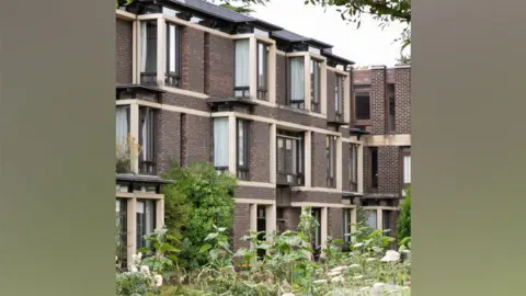 Historic England Archive A three storey 1980s college building of red brick and stone with plants in front, Fitzwilliam College, Cambridge