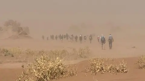 Family A line of people walking into the distance in a sandy landscape