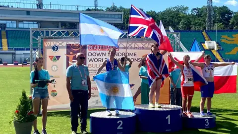 Family People stand up on a podium holding flags as they accept their medals.
