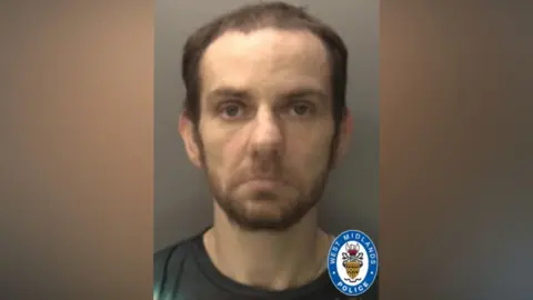 A mugshot of Philip McCarthy looking at the camera. He has brown facial hair and is wearing a grey top. The West Midlands Police logo is in the bottom right corner.
