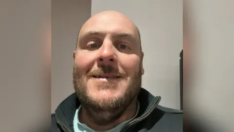 Dave Paltan Dave Paulton mostra um sorriso em uma selfie. Ele tem uma barba loira e é depois de um saltador de gola alta.