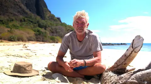 Channel 5 Broadcasting Limited Press Phillip Schofield sitting on a beach in Cast Away looking pensive in shorts and T-shirt 