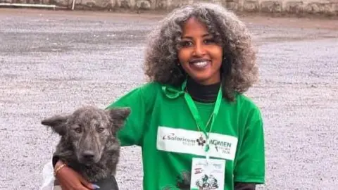 Feven Melese Feven Melese wears a green top and lanyard. She poses with her arm around a dog.