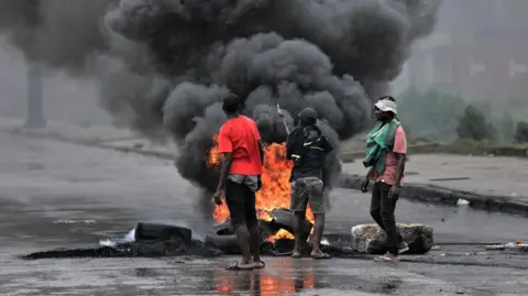 EPA A group of men stand on a road in front of burning tyres - with thick black smoke billowing upwards.