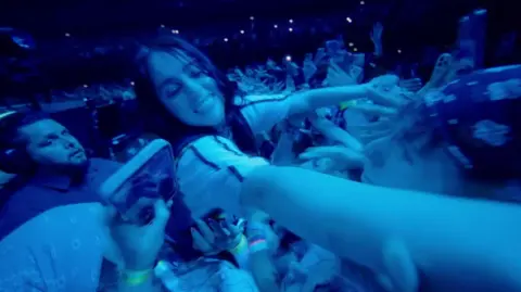 Paramount Pictures UK Eilish reaching into the crowd as they reach back at her while a nervous looking security guard watches on.