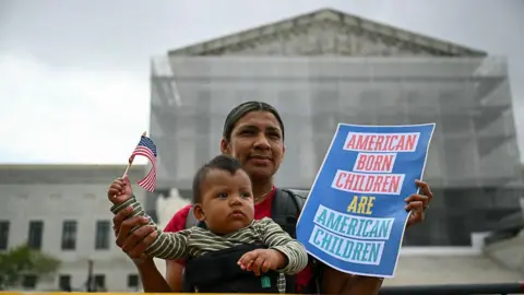 Getty Images A mother with her infant son hold a US flag and sign saying "American born children are American children" outside the US Supreme Court