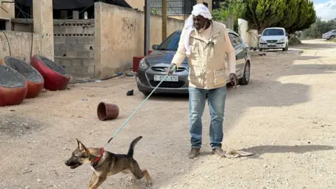 A man stands in a street with a dog straining on its leash