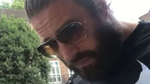 BBC A photograph  of Chris Harkins from his Tinder profile. He is extracurricular  with trees and houses successful  the background. He has his acheronian  hairsbreadth  slicked backmost  and a afloat  beard. He is wearing ample  tinted sunglasses with a bladed  metallic  rim. He is looking down   towards the ground. 